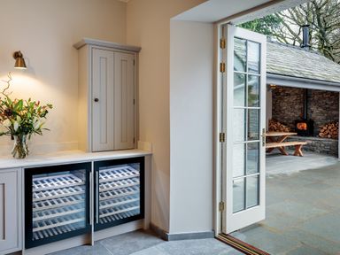 A kitchen corner with a flower vase on the counter and a glass door opening to an outdoor area with a wood stove and picnic table at The Vicarage near Rosthwaite
