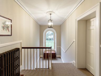 A hallway with carpeted floor a wooden chest a window and a hanging light at The Vicarage near Rosthwaite