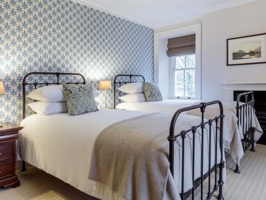 A bedroom with two metal frame single beds bedside table lamps and patterned wallpaper at The Vicarage near Rosthwaite
