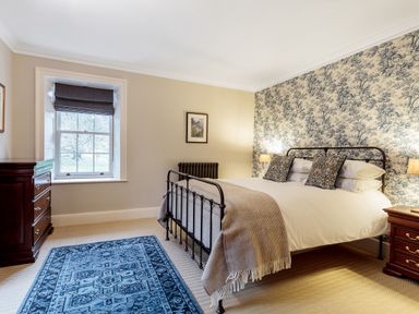 A bedroom with a metal bed frame blue rug and wooden furniture at The Vicarage near Rosthwaite