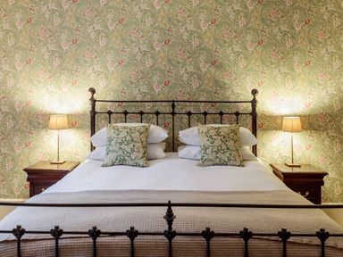 A bedroom with a metal bed frame two patterned pillows two bedside tables with lamps and floral wallpaper at The Vicarage near Rosthwaite