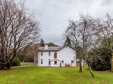 A white two-story house with several windows surrounded by leafless trees on a grassy lawn at The Vicarage near Rosthwaite