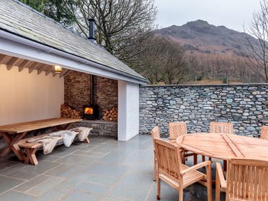 An outdoor patio with wooden tables and chairs and a covered area with a wood burning stove at The Vicarage near Rosthwaite