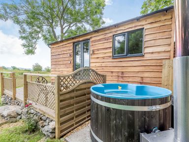 A wooden cabin with a deck and a blue hot tub outside at Stag Lodge Pod in Llanfair Caereinion