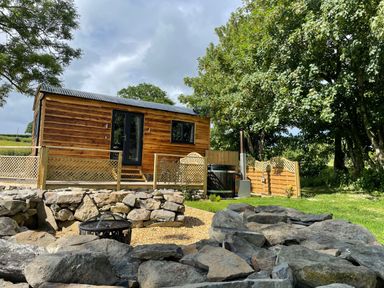 A wooden pod with a deck surrounded by a fenced garden and trees at Stag Lodge Pod in Llanfair Caereinion