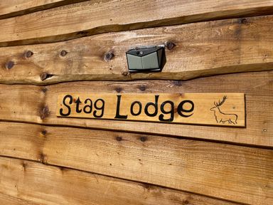 A wooden sign with the text Stag Lodge and a drawing of a stag on a wooden wall at Stag Lodge Pod in Llanfair Caereinion