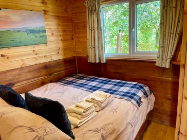 A bedroom with a bed towels and a window with curtains at Stag Lodge Pod in Llanfair Caereinion