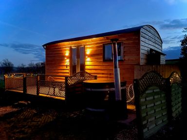 An exterior view of a wooden pod with lit lamps and a deck with lattice fencing at Stag Lodge Pod in Llanfair Caereinion