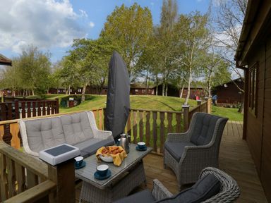 An outdoor wooden deck with rattan furniture including a table with croissants and coffee cups at Lakeland Dream at South Lakeland Leisure Lodge in Warton