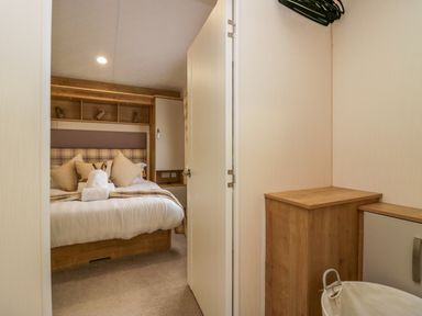 A bedroom with a bed white bedding pillows and shelves next to a wooden cabinet with hangers above at Lakeland Dream @ South Lakeland Leisure Lodge in Warton