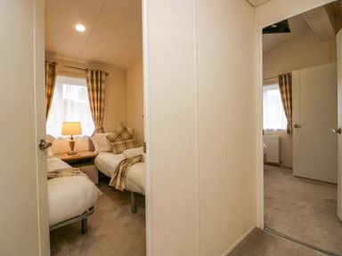 A hallway with doors leading to two bedrooms each with twin beds and plaid curtains at Lakeland Dream @ South Lakeland Leisure Lodge in Warton