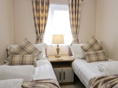 A bedroom with two single beds a wooden nightstand and a table lamp at Lakeland Dream @ South Lakeland Leisure Lodge in Warton