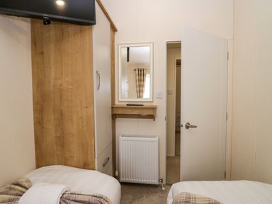 A bedroom with two single beds a wardrobe a wall-mounted tv a mirror and an open door at Lakeland Dream @ South Lakeland Leisure Lodge in Warton