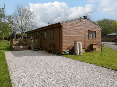 A wooden lodge with a gravel driveway and a small deck in a grassy area at Lakeland Dream @ South Lakeland Leisure Lodge in Warton