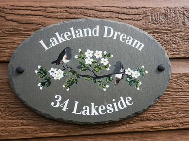 An oval sign with birds and flowers mounted on a wooden wall at Lakeland Dream @ South Lakeland Leisure Lodge in Warton