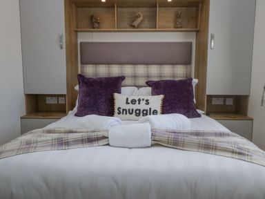 A bed with pillows and towels in a bedroom with wooden shelves at Lakeland Dream @ South Lakeland Leisure Lodge in Warton