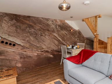 A living area with a grey sofa and red blanket near a wooden staircase and dining table against a rock wall at The Old Mill Bake House in Goodrich