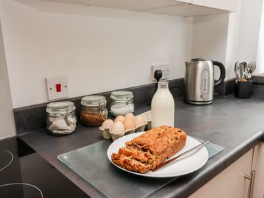 A kitchen counter with a loaf of bread on a plate a bottle of milk eggs in a carton jars of ingredients an electric kettle and cutlery at The Old Mill Bake House in Goodrich