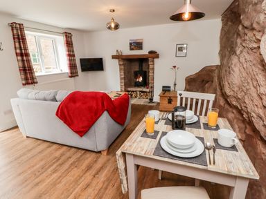 A living room with a dining table set with plates glasses and cutlery a grey sofa with a red throw a fireplace and a rock wall at The Old Mill Bake House in Goodrich