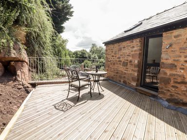 An outdoor wooden deck with metal table and two chairs next to a stone building at The Old Mill Bake House in Goodrich