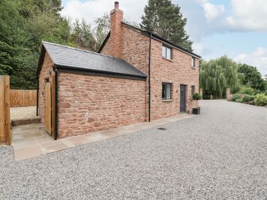 A stone house with a black door and windows surrounded by gravel and trees at The Old Mill Bake House in Goodrich