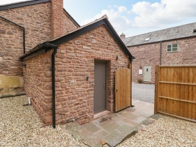 A stone building with a closed grey door and an open wooden gate on a gravel and stone patio at The Old Mill Bake House in Goodrich