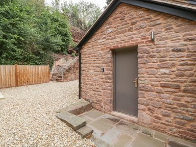 A gravel yard with stone steps leading to a timber fence and a stone building with a gray door at The Old Mill Bake House in Goodrich
