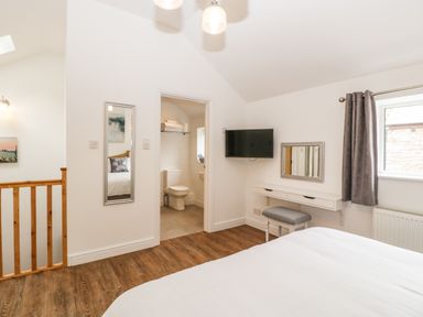 A bedroom with a bed a mounted television a dressing table with a stool a mirror and an open door to a bathroom at The Old Mill Bake House in Goodrich