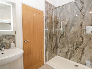 A bathroom with a shower area with glass screen sink with faucet wooden door and a mirror above the sink at The Old Mill Bake House in Goodrich