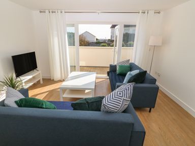 A living room with two blue sofas a white coffee table and a television near sliding glass doors at 3 Lon Y Dryw in Trearddur Bay