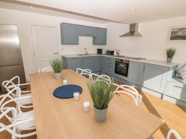 A kitchen with blue cabinets white chairs around a wooden dining table and stainless steel appliances at 3 Lon Y Dryw in Trearddur Bay