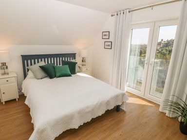 A bedroom with a bed with green pillows two bedside tables with lamps and glass doors leading outside at 3 Lon Y Dryw in Trearddur Bay
