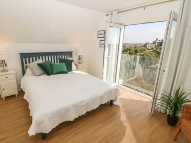 A bedroom with a bed green pillows bedside tables lamps and an open glass door leading to a balcony at 3 Lon Y Dryw in Trearddur Bay