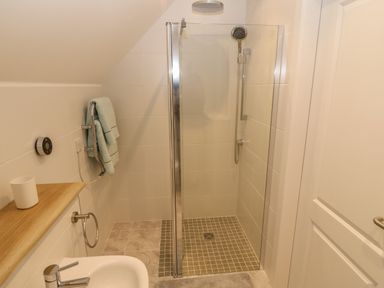 A bathroom with a walk-in shower a glass partition towels on a rack and a sink at 3 Lon Y Dryw in Trearddur Bay