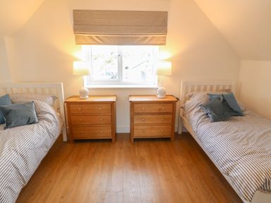 A bedroom with two single beds with striped bedding and pillows separated by two wooden nightstands and lamps at 3 Lon Y Dryw in Trearddur Bay