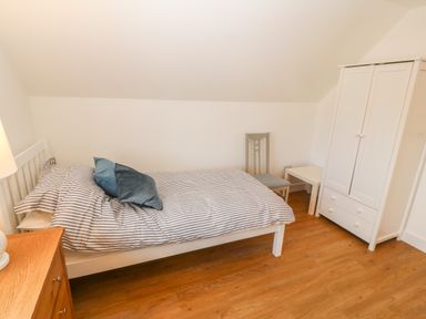 A bedroom with a bed and striped bedding a chair a white wardrobe and wooden flooring at 3 Lon Y Dryw in Trearddur Bay