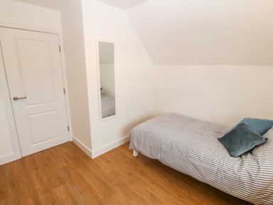 A bedroom with a single bed with striped bedding two pillows a full length mirror and a white door at 3 Lon Y Dryw in Trearddur Bay