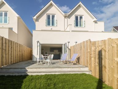 A backyard patio with white metal chairs and table and striped deck chairs at 3 Lon Y Dryw in Trearddur Bay