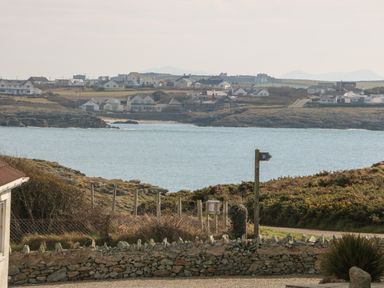 A coastal view with houses across the water and a stone wall with a signpost in the foreground at 3 Lon Y Dryw in Trearddur Bay