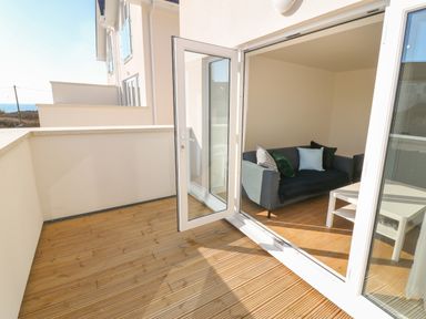 A balcony with wooden floor and open glass door leading to a living room with a sofa and coffee table at 3 Lon Y Dryw in Trearddur Bay