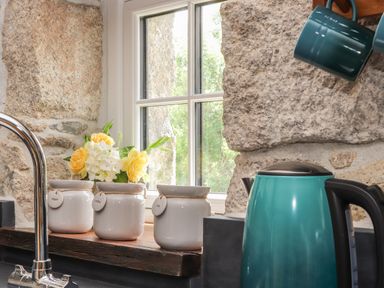 A kitchen window with jars labeled sugar coffee and tea a kettle and mugs hanging at The Hayloft in Helston