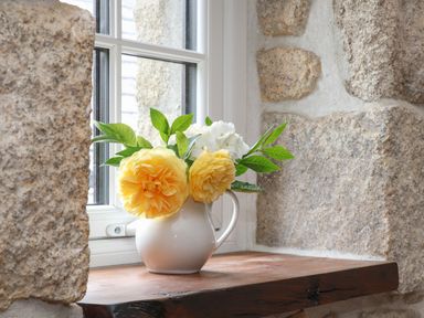A white ceramic jug with yellow and white flowers on a wooden windowsill with stone walls at The Hayloft in Helston