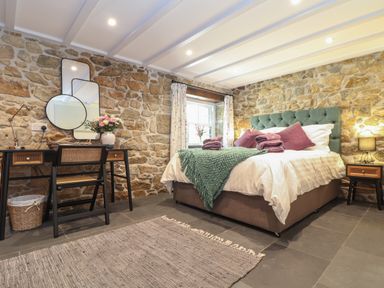 A bedroom with a stone wall bed table chair and mirrors at The Hayloft in Helston