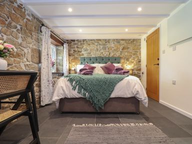 A bedroom with a bed against a stone wall and a wooden door at The Hayloft in Helston