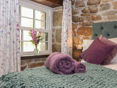 A bedroom with a window flowers in a vase rolled towels and pillows on a bed with a knitted throw at The Hayloft in Helston