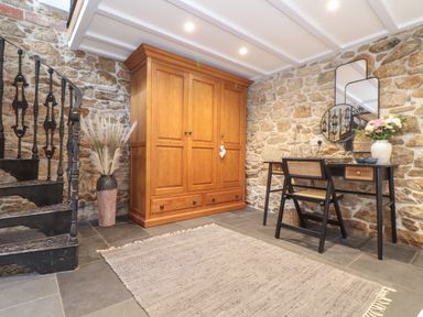 A room with a wooden wardrobe black spiral staircase desk and chair against stone walls at The Hayloft in Helston