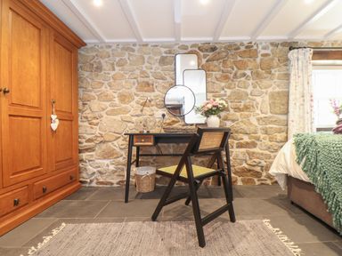 A room with a wooden wardrobe stone wall a desk with three mirrors a chair and a bed at The Hayloft in Helston
