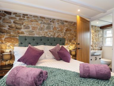 A bedroom with a stone wall and a bed with purple pillows and towels and a green knit blanket at The Hayloft in Helston