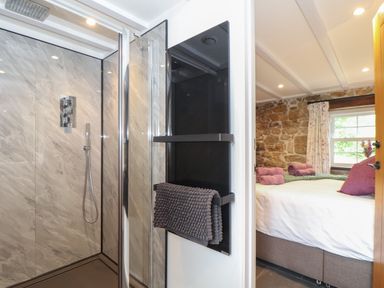 A bathroom with a shower and a towel rack next to a bedroom with a bed and stone wall at The Hayloft in Helston