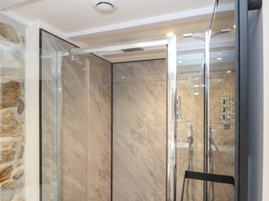A shower enclosure with marble effect walls and a glass door next to a stone wall at The Hayloft in Helston